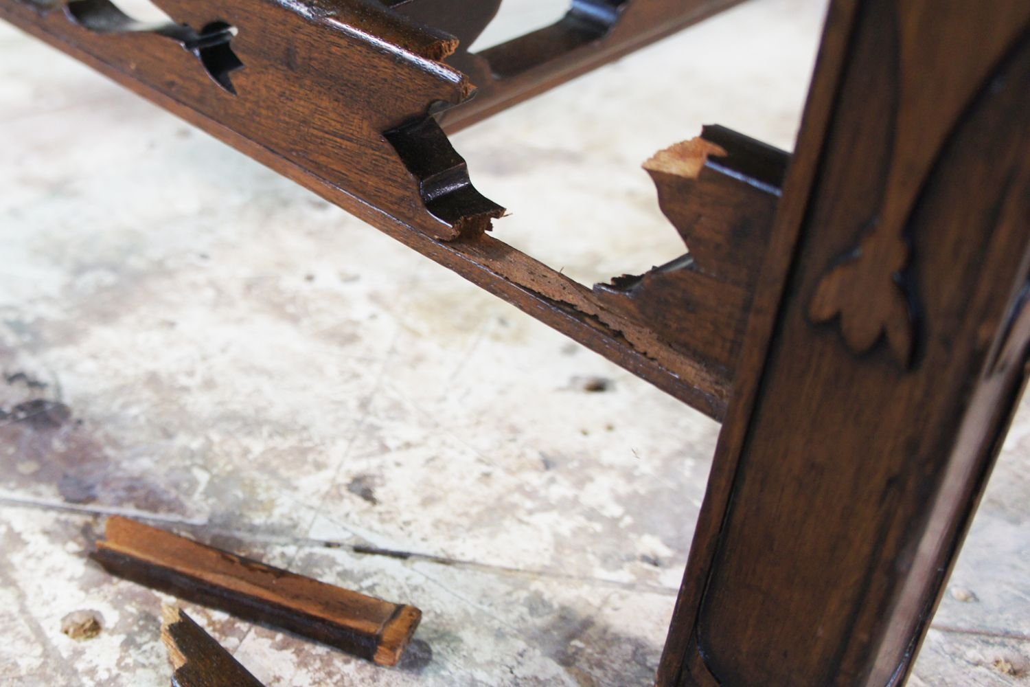 A wooden chair displaying a broken piece of wood on one of its legs, indicating damage and wear.