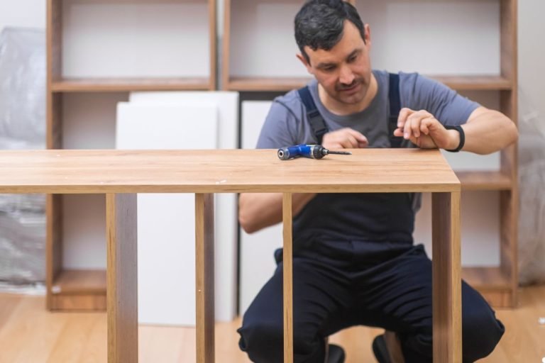 A man using a drill while working at a table, focused on his task in a well-lit workshop environment.