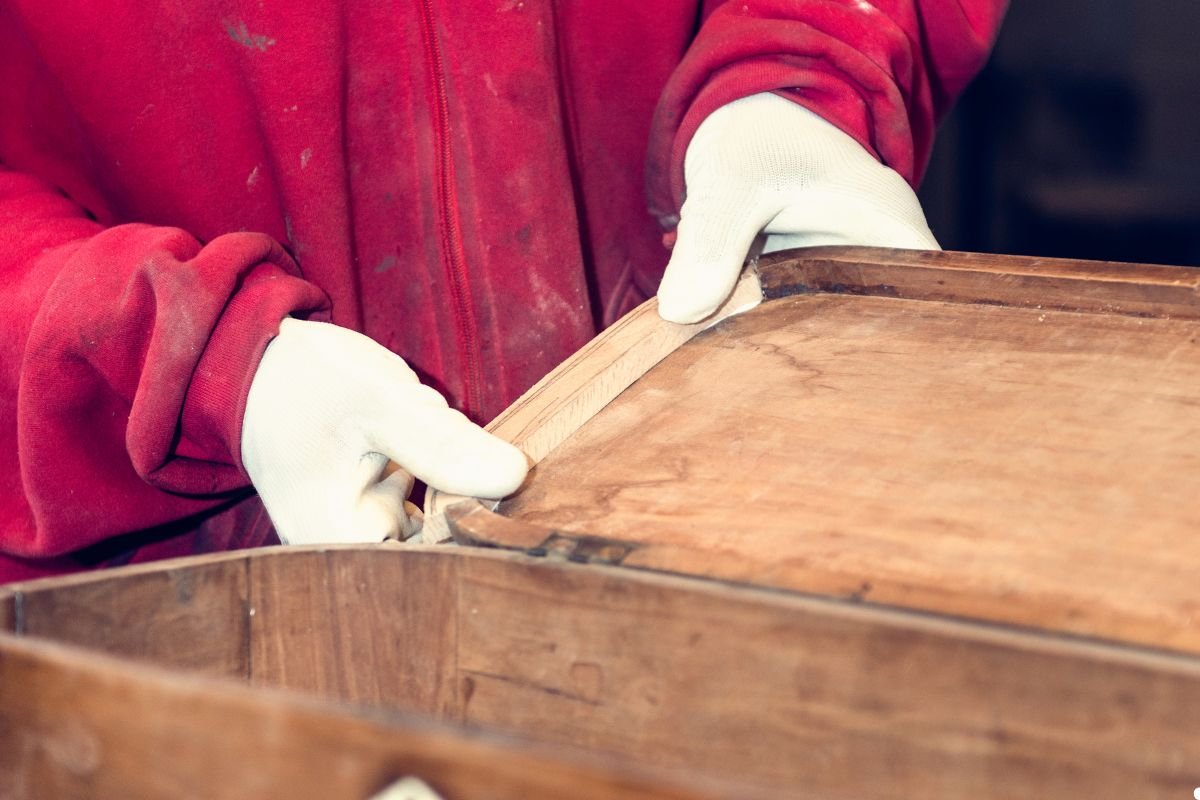 A person wearing a red jacket holds a wooden box, standing against a neutral background.